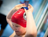 Ein lächelndes Kind mit Badekappe setzt sich die Schwimmbrille auf.